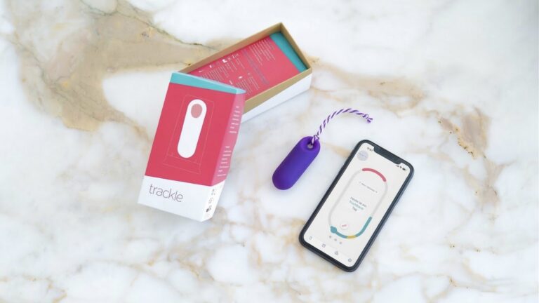 Das trackle Sensorsystem neben seiner Verpackung und einem Smartphone, das die zugehörige Zyklus-App mit Zyklusdaten anzeigt.
